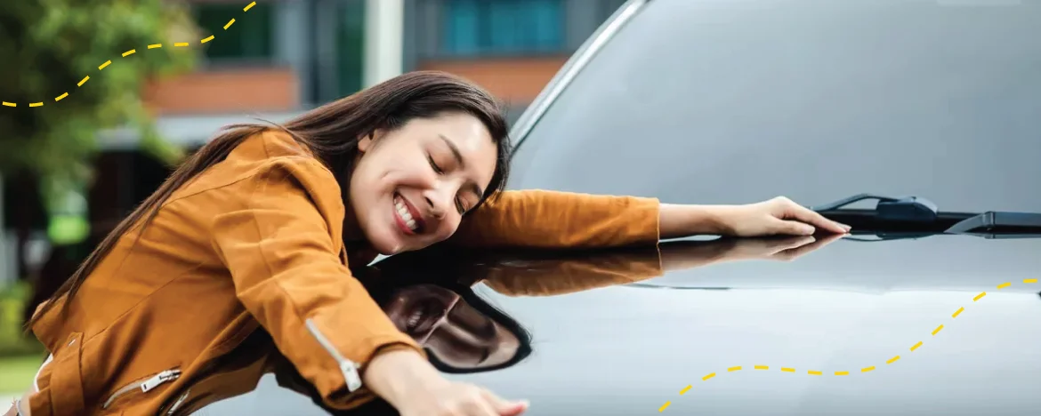 A happy woman hugs the bonnet of her car