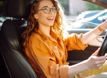 Smiling woman in orange shirt driving a car